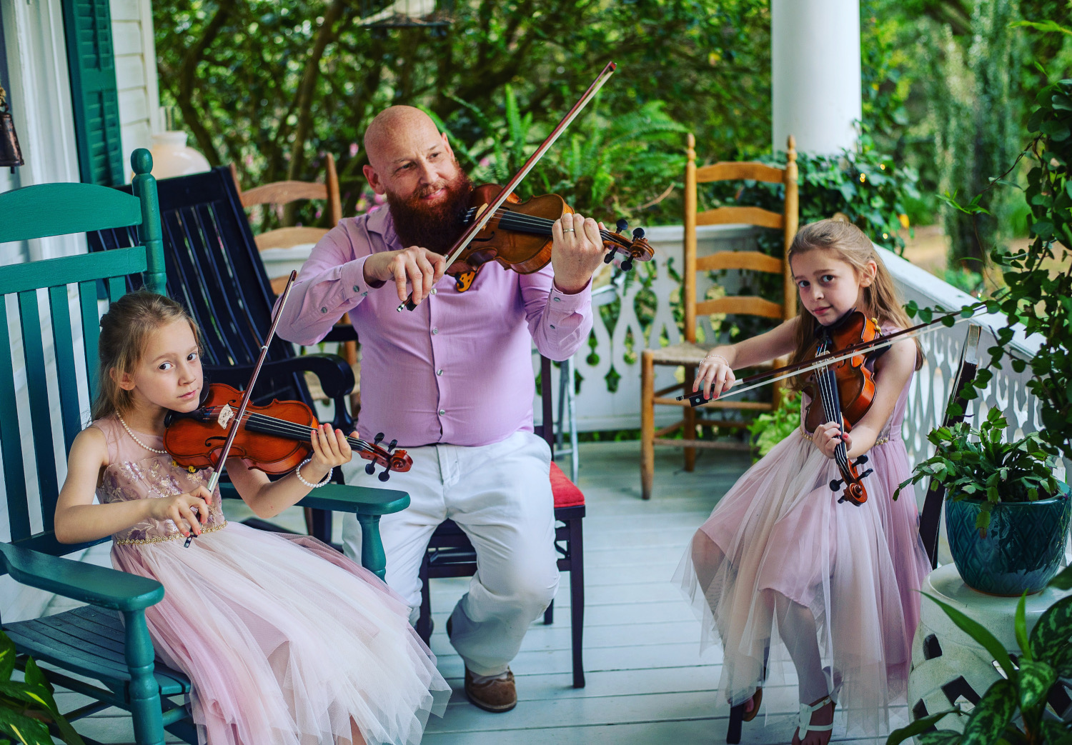 Fiddlin Fluds posed on porch positioned to play the fiddles