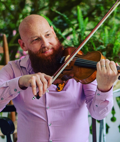 John posing with a smile positioned to play fiddle.